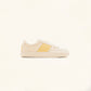 Vue latérale de la basket posée sur un fond clair, présentant son design épuré et ses détails artisanaux.
La silhouette minimaliste met en valeur la combinaison du tissu beige et des broderies jaunes